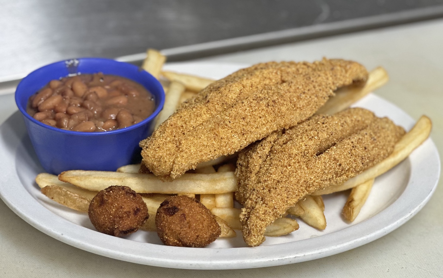 Fried fish with fries, pinto beans, and hush puppies